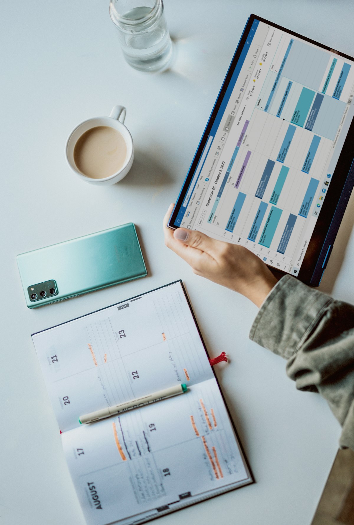 A hand writing in a weekly planner at a desk