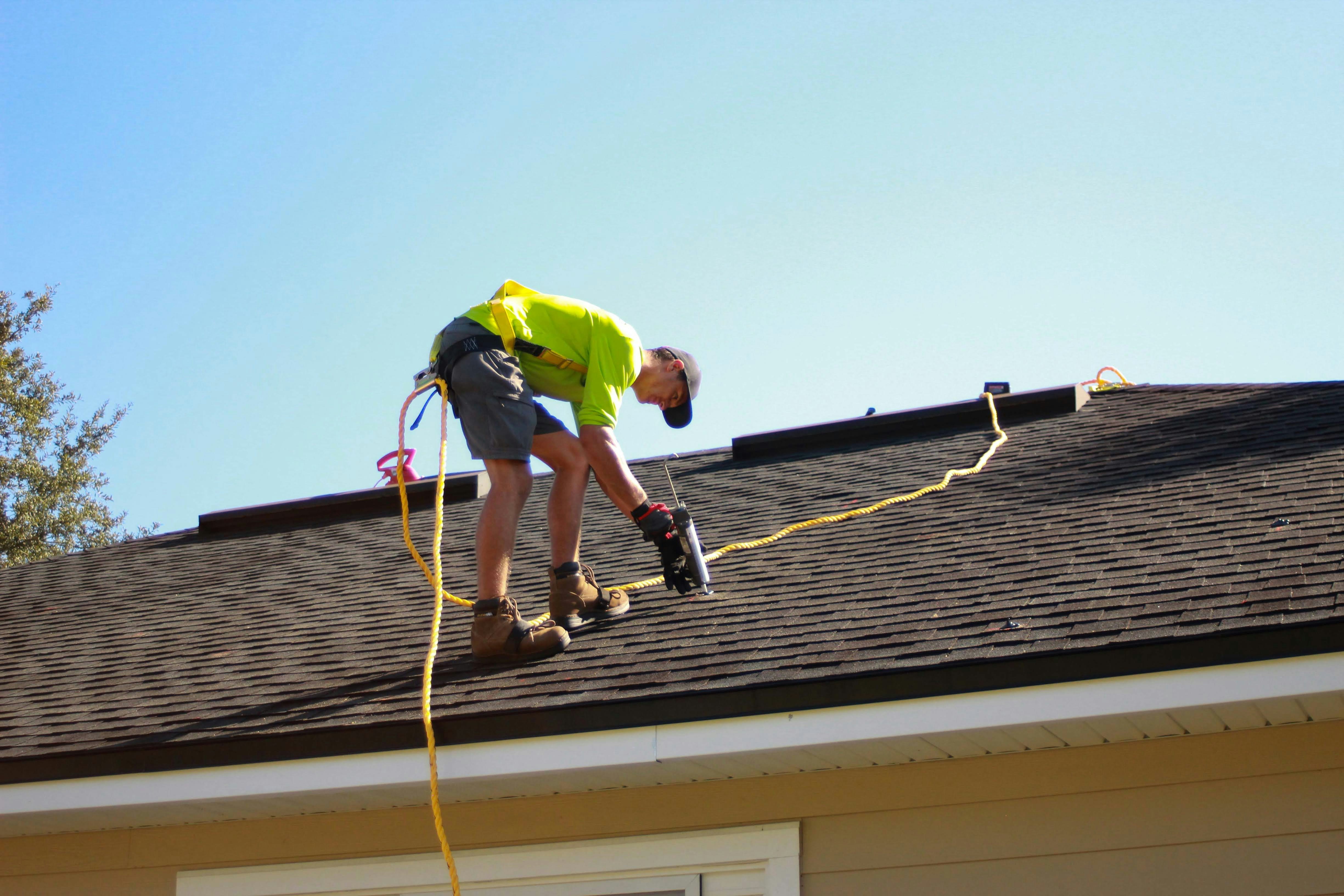 Roofer working on a shingled roof under a blue sky